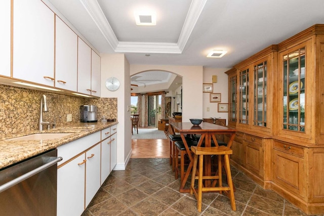 kitchen featuring stainless steel dishwasher, dark tile flooring, sink, light stone countertops, and a tray ceiling