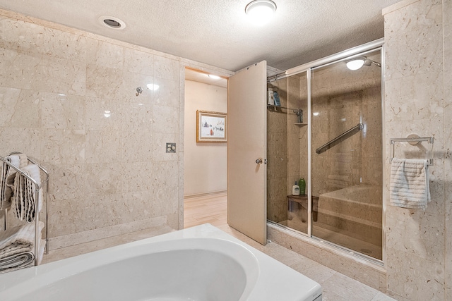 bathroom featuring independent shower and bath, tile walls, tile floors, and a textured ceiling