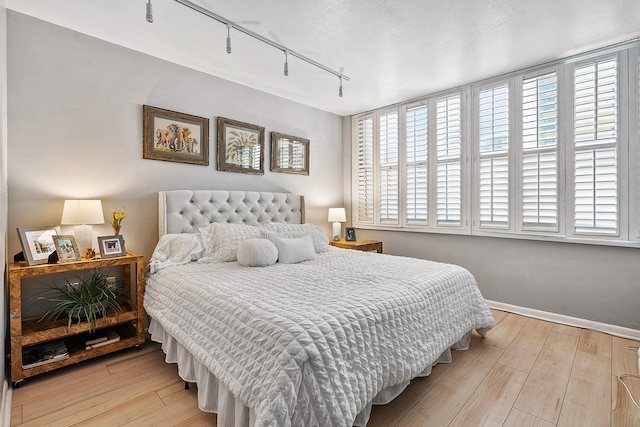 bedroom featuring light hardwood / wood-style floors, a textured ceiling, track lighting, and multiple windows