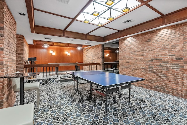 rec room with coffered ceiling, wooden walls, dark tile floors, and brick wall