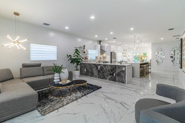 kitchen with wall chimney range hood, kitchen peninsula, decorative light fixtures, white cabinetry, and stainless steel refrigerator