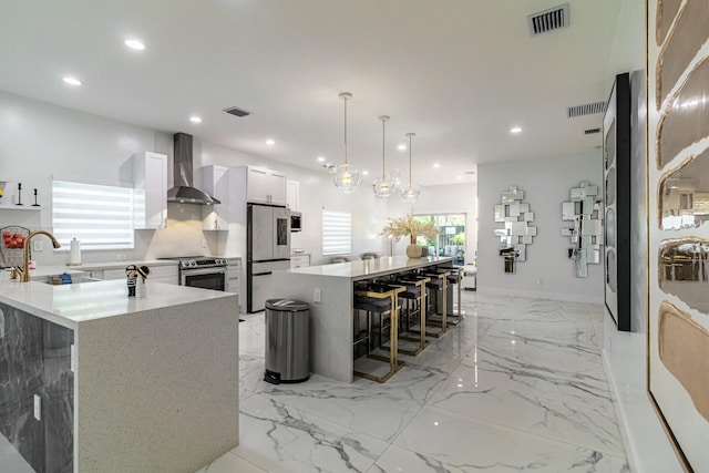 kitchen with stainless steel appliances, a breakfast bar, a sink, visible vents, and wall chimney range hood