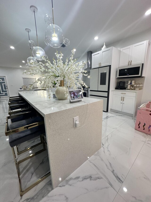 kitchen with stainless steel refrigerator, light stone countertops, white cabinetry, wall chimney exhaust hood, and hanging light fixtures