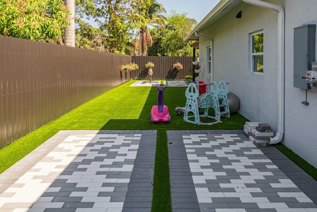 view of yard with electric panel, a fenced backyard, and a patio