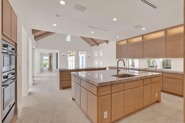 kitchen with light stone countertops, a kitchen island with sink, sink, a wealth of natural light, and lofted ceiling with beams