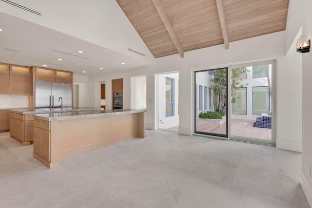 kitchen with an island with sink, stainless steel built in refrigerator, light stone countertops, and light tile floors