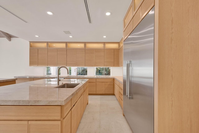 kitchen featuring light brown cabinetry, an island with sink, built in refrigerator, sink, and light tile floors