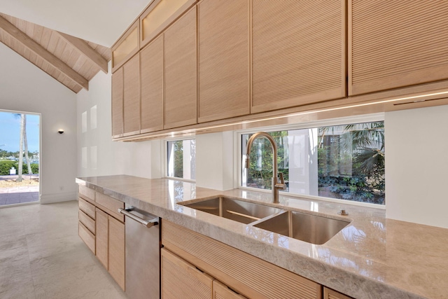 kitchen featuring high vaulted ceiling, light stone countertops, light brown cabinetry, dishwasher, and sink