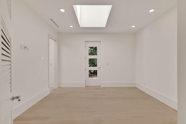 unfurnished room with a skylight and light hardwood / wood-style floors