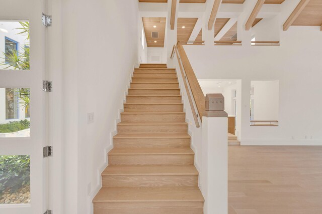 staircase featuring light wood-type flooring, a towering ceiling, and beam ceiling