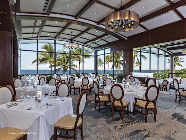 dining room featuring coffered ceiling, an inviting chandelier, a water view, dark colored carpet, and lofted ceiling with beams