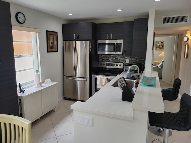 kitchen featuring stainless steel appliances, light tile floors, a kitchen bar, backsplash, and sink