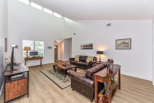 living room featuring high vaulted ceiling, a textured ceiling, and light wood-type flooring