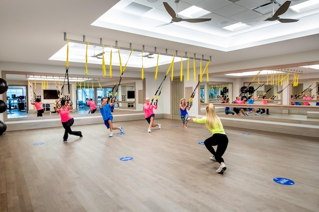 workout area with ceiling fan, a tray ceiling, and wood-type flooring