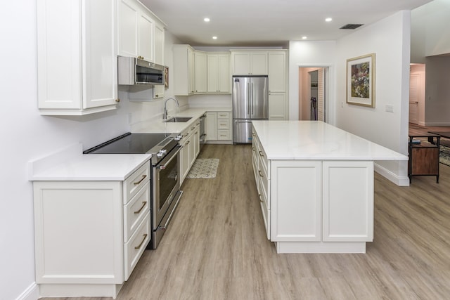 kitchen featuring stainless steel appliances, sink, white cabinets, light wood-type flooring, and a kitchen island