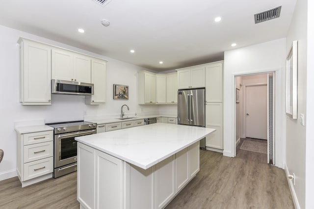 kitchen with stainless steel appliances, sink, a center island, light hardwood / wood-style flooring, and light stone countertops