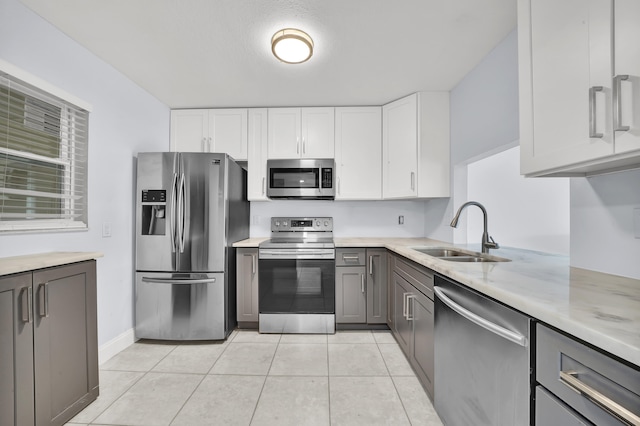 kitchen with appliances with stainless steel finishes, sink, light tile patterned floors, gray cabinets, and white cabinetry