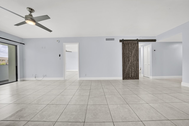 tiled spare room featuring a barn door and ceiling fan