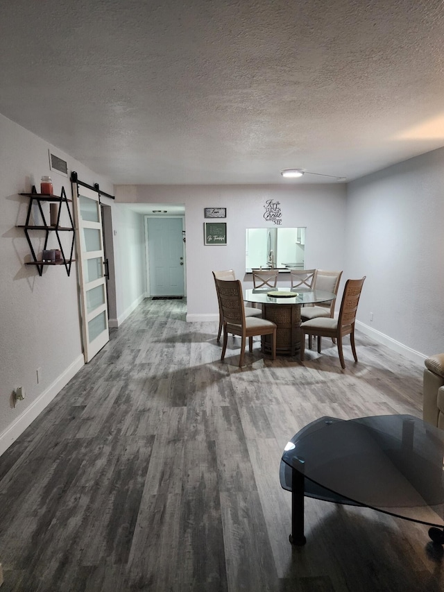 dining space featuring a barn door, wood-type flooring, and a textured ceiling