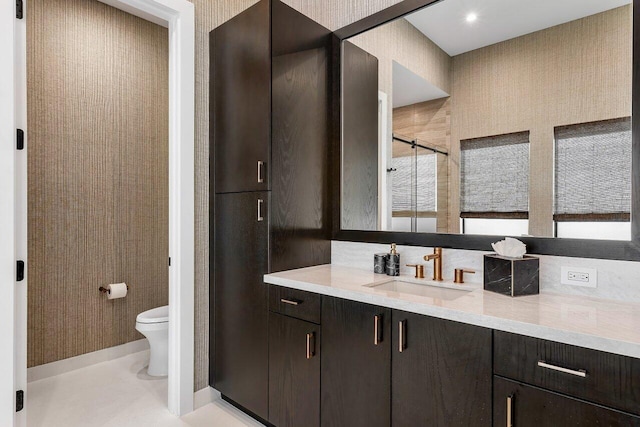 bathroom featuring toilet, vanity, and a shower with door