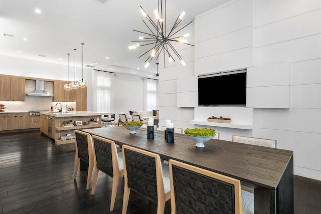 kitchen featuring tasteful backsplash, wall chimney range hood, an island with sink, decorative light fixtures, and dark hardwood / wood-style floors