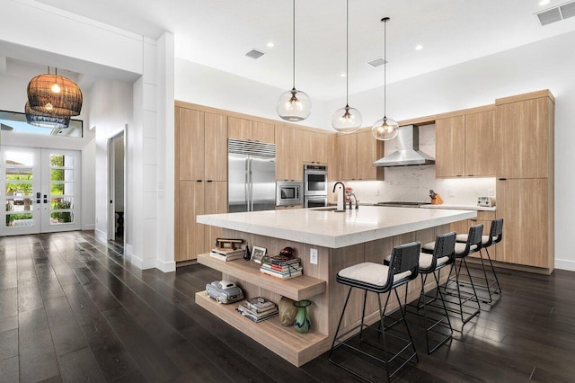 kitchen featuring wall chimney range hood, dark hardwood / wood-style flooring, built in appliances, and an island with sink