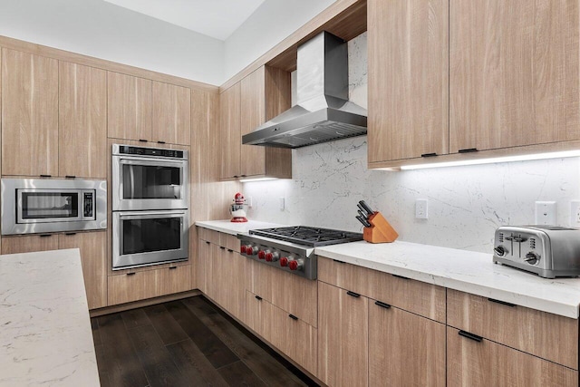 kitchen featuring wall chimney range hood, light brown cabinets, light stone countertops, dark hardwood / wood-style floors, and stainless steel appliances