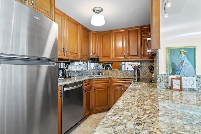 kitchen featuring tasteful backsplash, light stone counters, brown cabinets, stainless steel appliances, and a sink