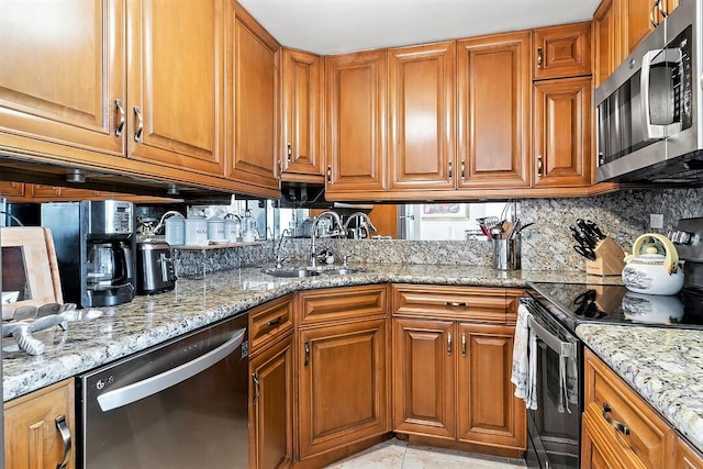 kitchen with light stone counters, a sink, appliances with stainless steel finishes, decorative backsplash, and brown cabinetry