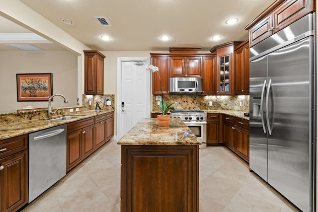 kitchen featuring sink, appliances with stainless steel finishes, a center island, light stone countertops, and decorative backsplash