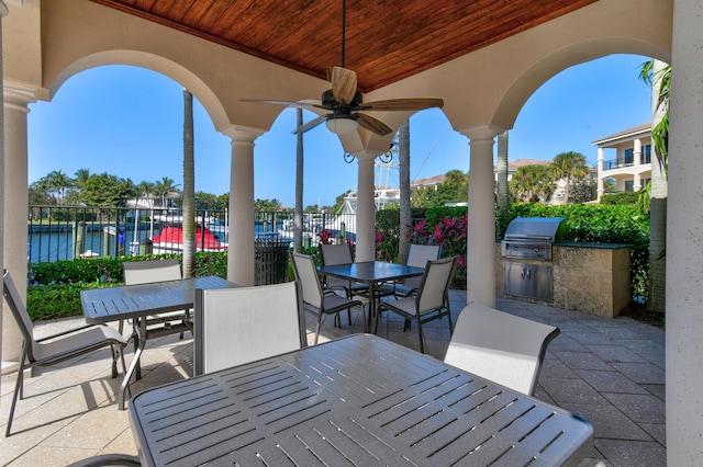 view of patio with exterior kitchen, a water view, a grill, and ceiling fan