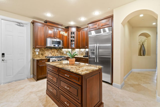 kitchen with light stone countertops, decorative backsplash, stainless steel appliances, and a kitchen island