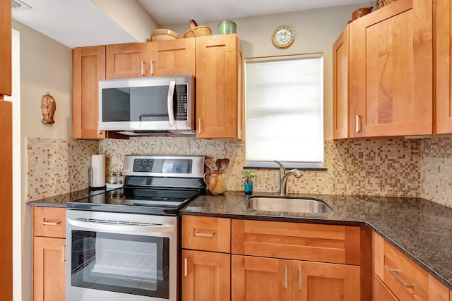 kitchen featuring stainless steel appliances, tasteful backsplash, dark stone counters, and sink