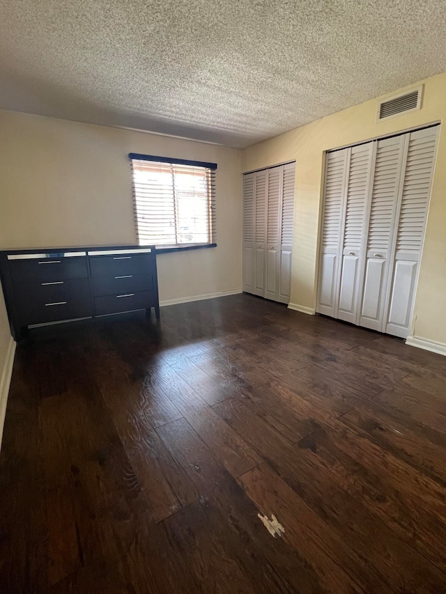 unfurnished bedroom with two closets, dark wood-type flooring, and a textured ceiling