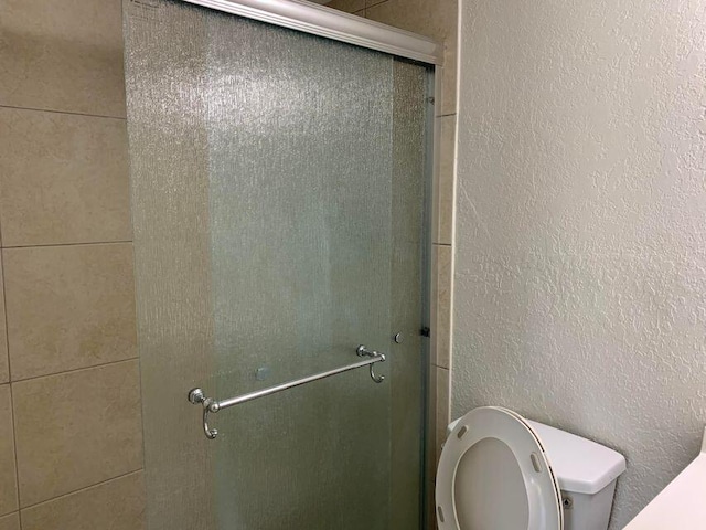 bathroom featuring toilet and a shower with shower door