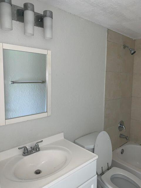 full bathroom featuring vanity, a textured ceiling, toilet, and tiled shower / bath