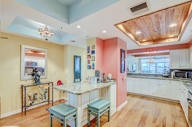 kitchen with a kitchen bar, light wood-type flooring, a raised ceiling, pendant lighting, and white cabinets