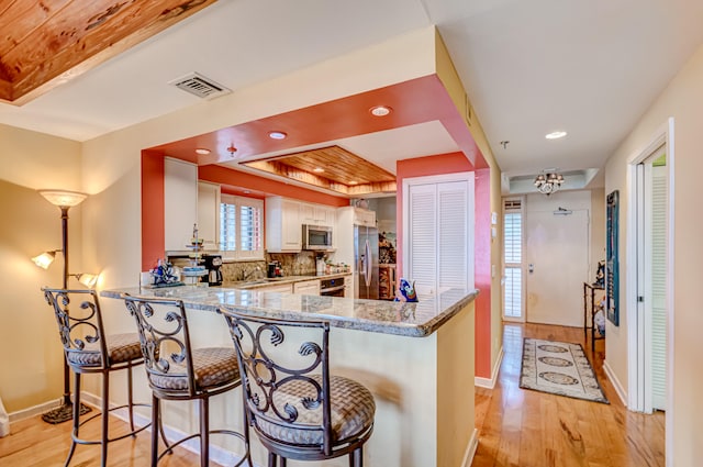 kitchen with white cabinetry, light stone counters, kitchen peninsula, a breakfast bar, and appliances with stainless steel finishes