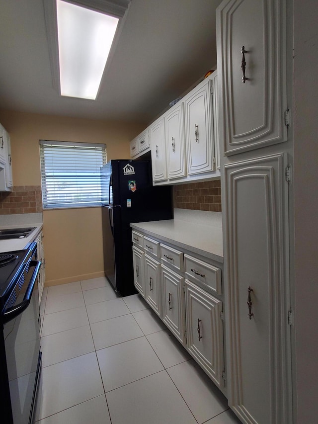 kitchen with light tile floors, range with electric stovetop, white cabinetry, and backsplash