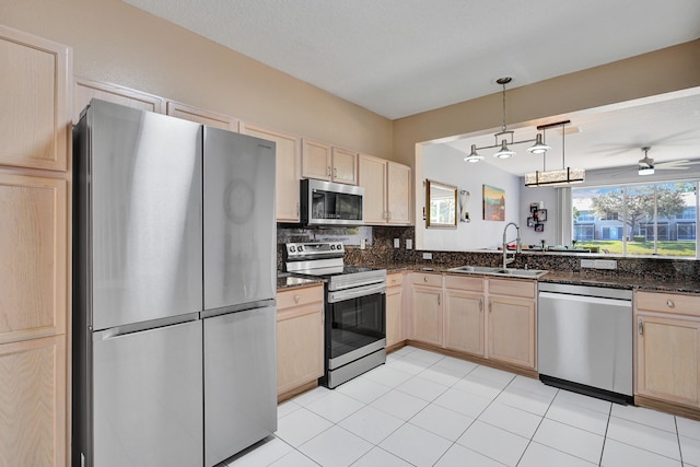 kitchen featuring stainless steel appliances, tasteful backsplash, light brown cabinetry, a sink, and dark stone counters