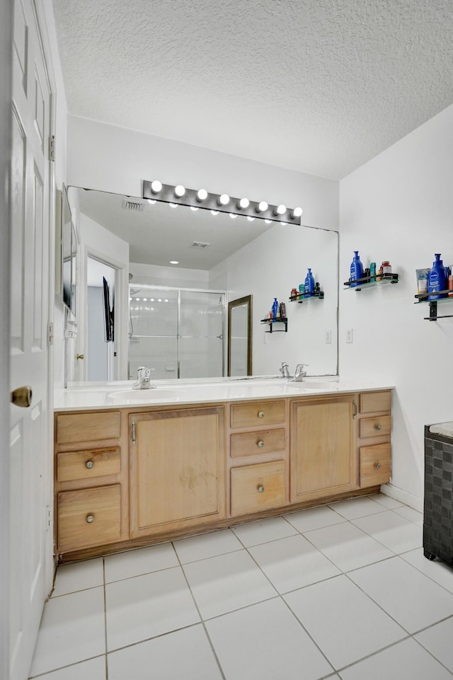 full bathroom with a textured ceiling, a sink, tile patterned floors, double vanity, and a stall shower