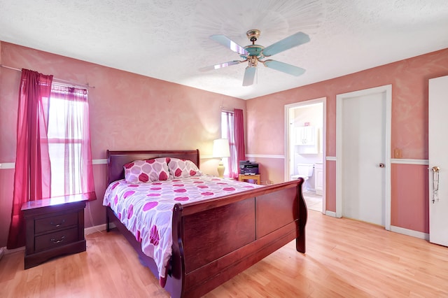 bedroom with ceiling fan, light hardwood / wood-style flooring, a textured ceiling, and connected bathroom