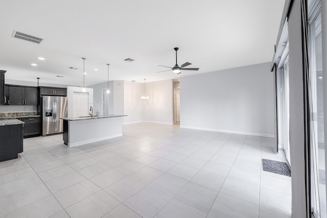 kitchen featuring light stone countertops, sink, stainless steel fridge, an island with sink, and ceiling fan with notable chandelier