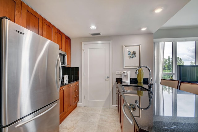 kitchen featuring appliances with stainless steel finishes, tasteful backsplash, sink, light tile patterned floors, and dark stone countertops