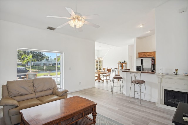 living room with lofted ceiling, ceiling fan with notable chandelier, and light wood-type flooring