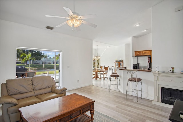 living room with light hardwood / wood-style floors, ceiling fan with notable chandelier, and lofted ceiling