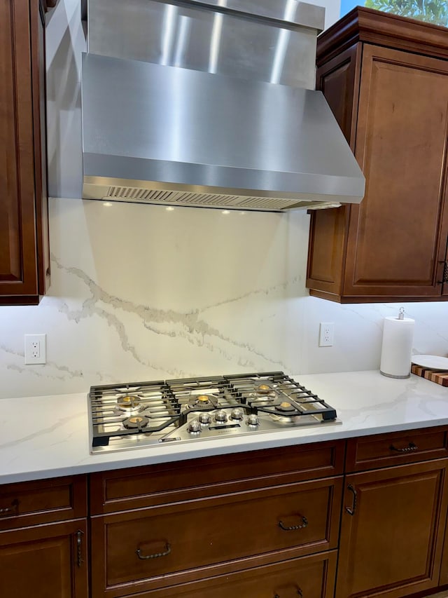 kitchen with light stone countertops, backsplash, stainless steel gas stovetop, and wall chimney exhaust hood