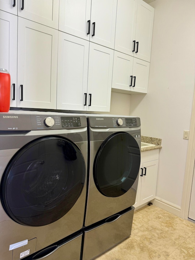 laundry area with light tile flooring, washing machine and dryer, and cabinets