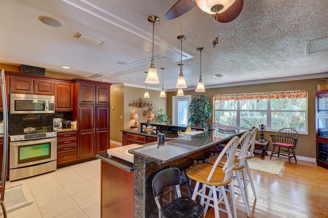 kitchen with hanging light fixtures, decorative backsplash, a breakfast bar, light hardwood / wood-style floors, and range with electric cooktop