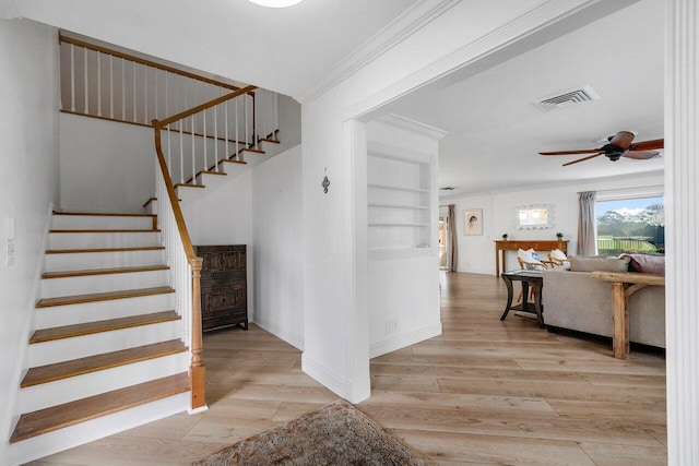 stairs with built in shelves, ceiling fan, wood-type flooring, and ornamental molding